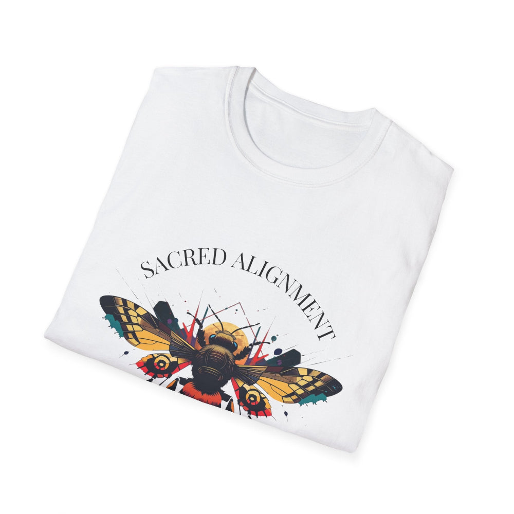 White folded unisex cotton t-shirt featuring bold "Sacred Alignment" graphic print: vibrant abstract bee with detailed wings and body, colorful geometric accents, and dynamic paint splatters in red, orange, teal, blue, and gold tones bursting outward around an orange moon background. Arched white text "SACRED ALIGNMENT" above. Motivational spiritual empowerment crewneck tee flat lay.