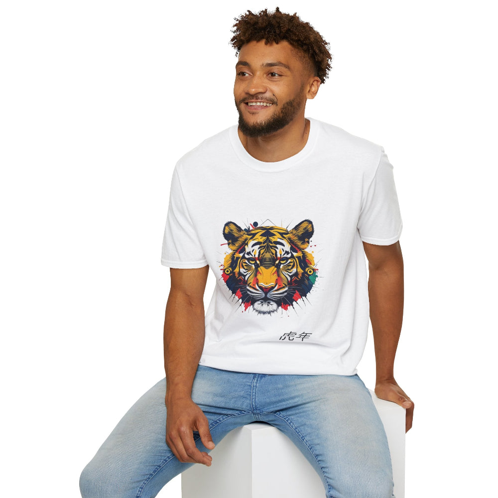 White unisex cotton t-shirt modeled by smiling man with curly hair and beard, featuring bold Year of the Tiger graphic: vibrant abstract tiger face portrait with fierce eyes, large stripes, geometric patterns, and dynamic multicolored paint splatters in yellow, orange, red, blue, and black tones exploding outward. Chinese text "虎年" (Year of the Tiger) printed below in black. Zodiac Chinese New Year motivational crewneck tee.