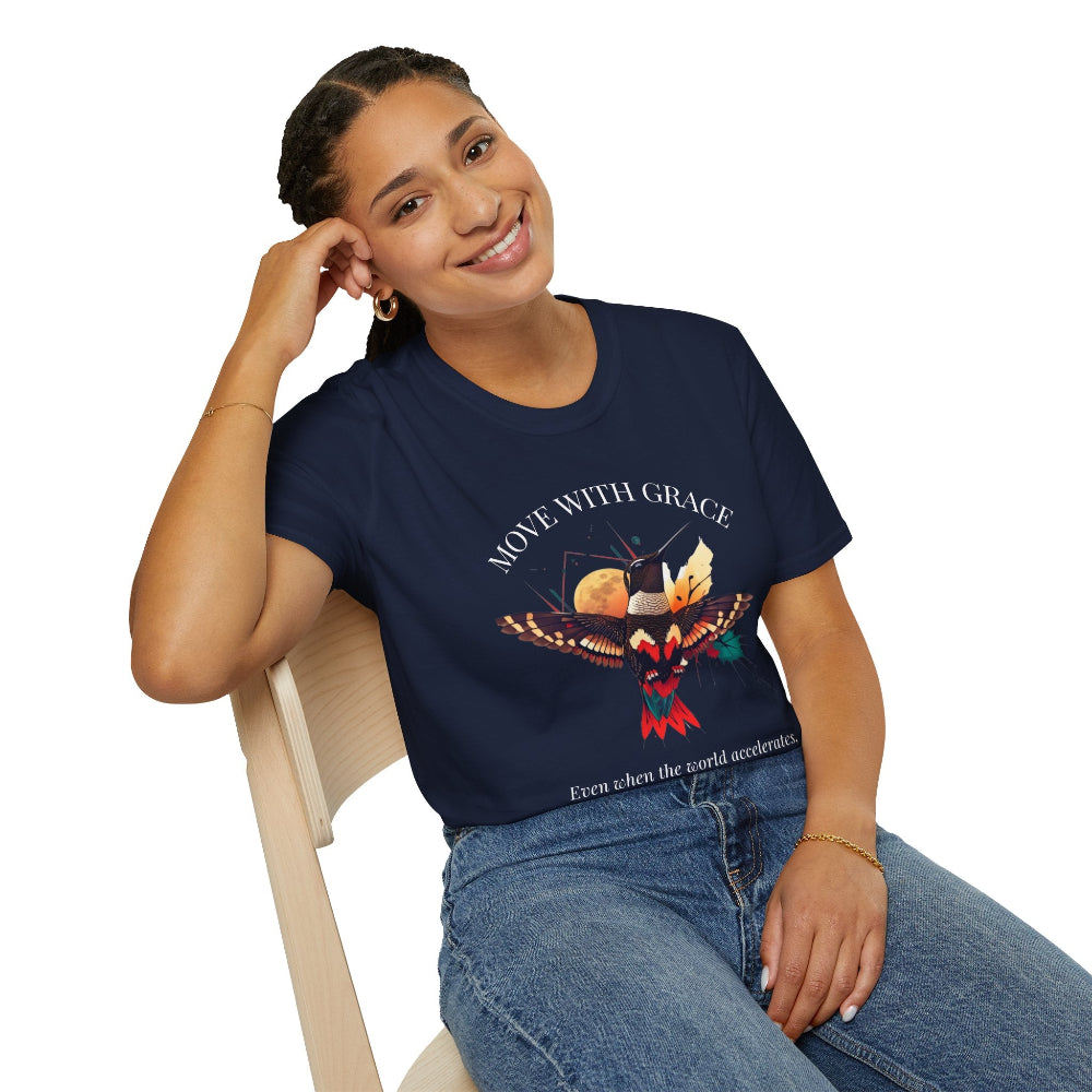 Woman wearing a navy blue t-shirt with a vibrant hummingbird graphic, "MOVE WITH GRACE" text above, and the quote "Even when the world accelerates, Your center remains steady" below. Casual motivational apparel paired with blue jeans.
