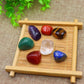 Set of 7 polished tumbled healing crystals on bamboo tray: amethyst, carnelian, tiger's eye, green aventurine, clear quartz, red jasper, lapis lazuli, natural gemstones for chakra balancing and meditation, zen display with green leaves background