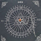 Spirit board divination chart (灵摆表) with a silver pendulum featuring a polished orange-red stone resting in the center. The circular wheel displays letters A-Z, numbers 0-9, "YES" and "NO", and a Star of David symbol, framed with ornate white corner decorations on a black background. Divination and dowsing tool.