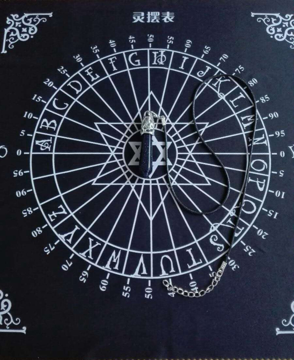 Black spirit board chart (灵摆表) with a dark blue stone pendulum resting in the center. The circular wheel features letters A-Z, numbers 0-9, "YES" and "NO", and a central Star of David symbol, framed with ornate white corner decorations. Divination and dowsing tool.