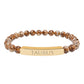 Bracelet with polished leopard jasper beads in earthy brown tones with natural veining, featuring a gold-plated curved bar engraved "TAURUS" in uppercase letters. Stretch-fit zodiac-inspired crystal jewelry.