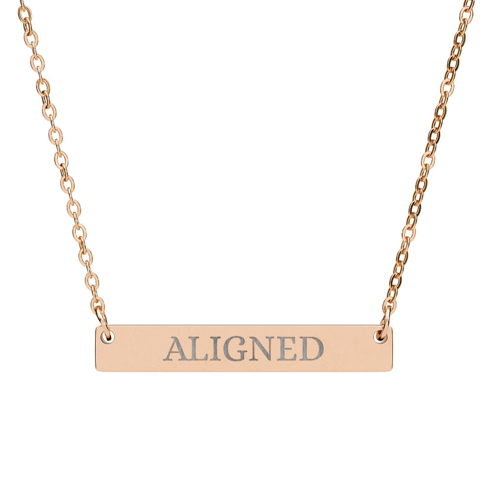 Rose gold bar necklace with engraved uppercase text "ALIGNED" on a sleek matte pendant, suspended on a delicate matching rose gold chain. Minimalist motivational affirmation jewelry for alignment, balance, and spiritual harmony.