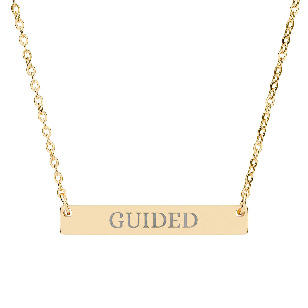 Gold bar necklace with engraved uppercase text "GUIDED" on a sleek matte pendant, suspended on a delicate matching gold chain. Minimalist motivational affirmation jewelry for guidance, intuition, and spiritual alignment.