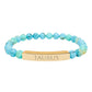 Bracelet with polished turquoise beads in soft aqua-blue tones with natural veining and speckles, featuring a gold-plated curved bar engraved "TAURUS" in uppercase letters. Stretch-fit zodiac-inspired crystal jewelry.