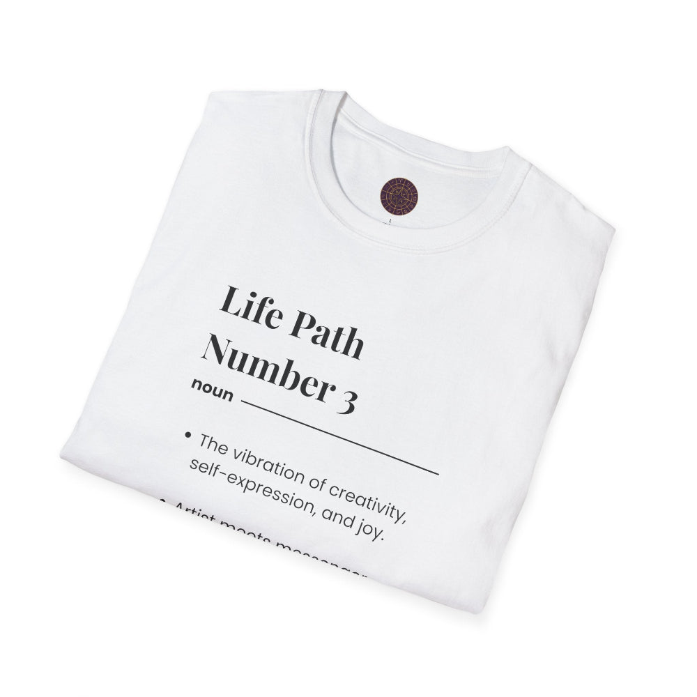 White folded unisex cotton t-shirt featuring bold Life Path Number 3 numerology print: dictionary-style definition text reading "Life Path Number 3 noun · The vibration of creativity, self-expression, and joy. · Artist/messenger energy — here to uplift, inspire, and speak truth with style. – see also: create, express, inspire". Motivational spiritual numerology crewneck tee flat lay with visible purple/gold zodiac wheel inner tag.