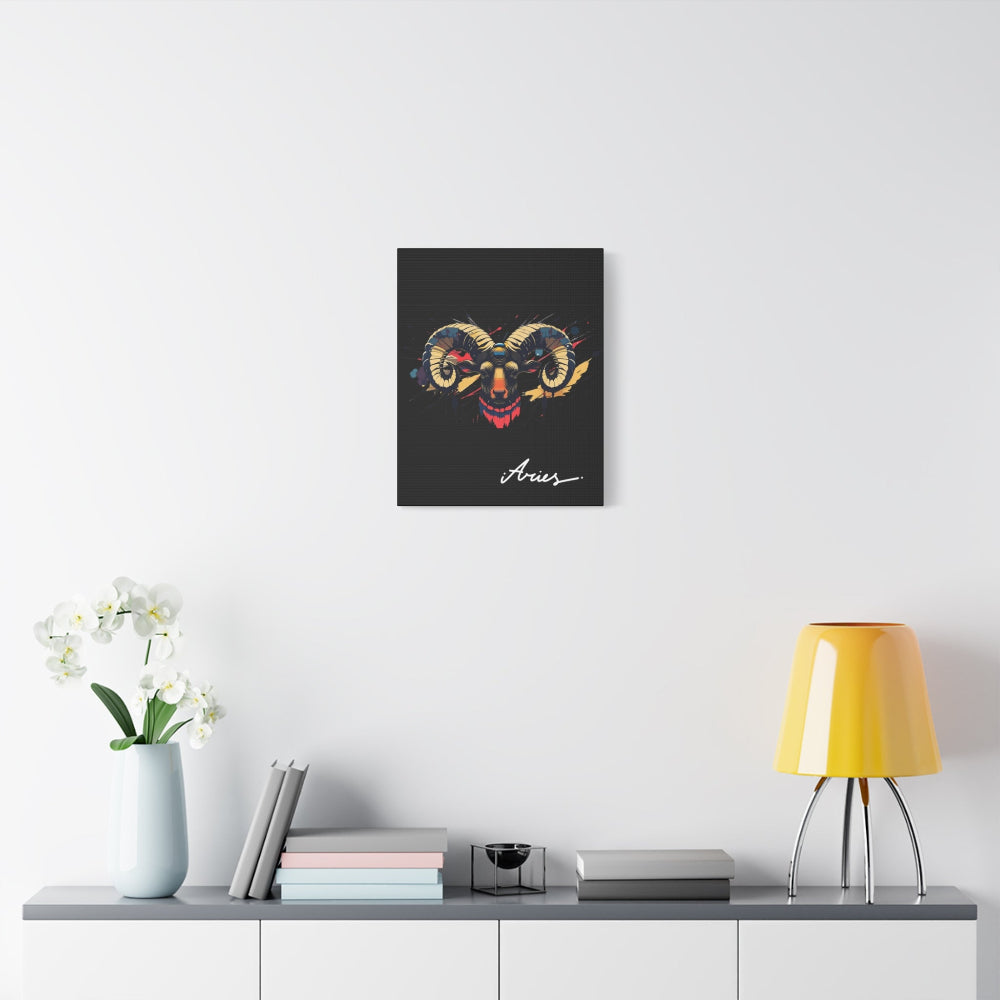 Black canvas wall art print of colorful abstract Aries ram head with curved horns, intense eyes, geometric patterns, and cosmic splatters on dark background, featuring "Aries" in elegant white cursive displayed in a modern home décor setting above a console table with books and yellow lamp.