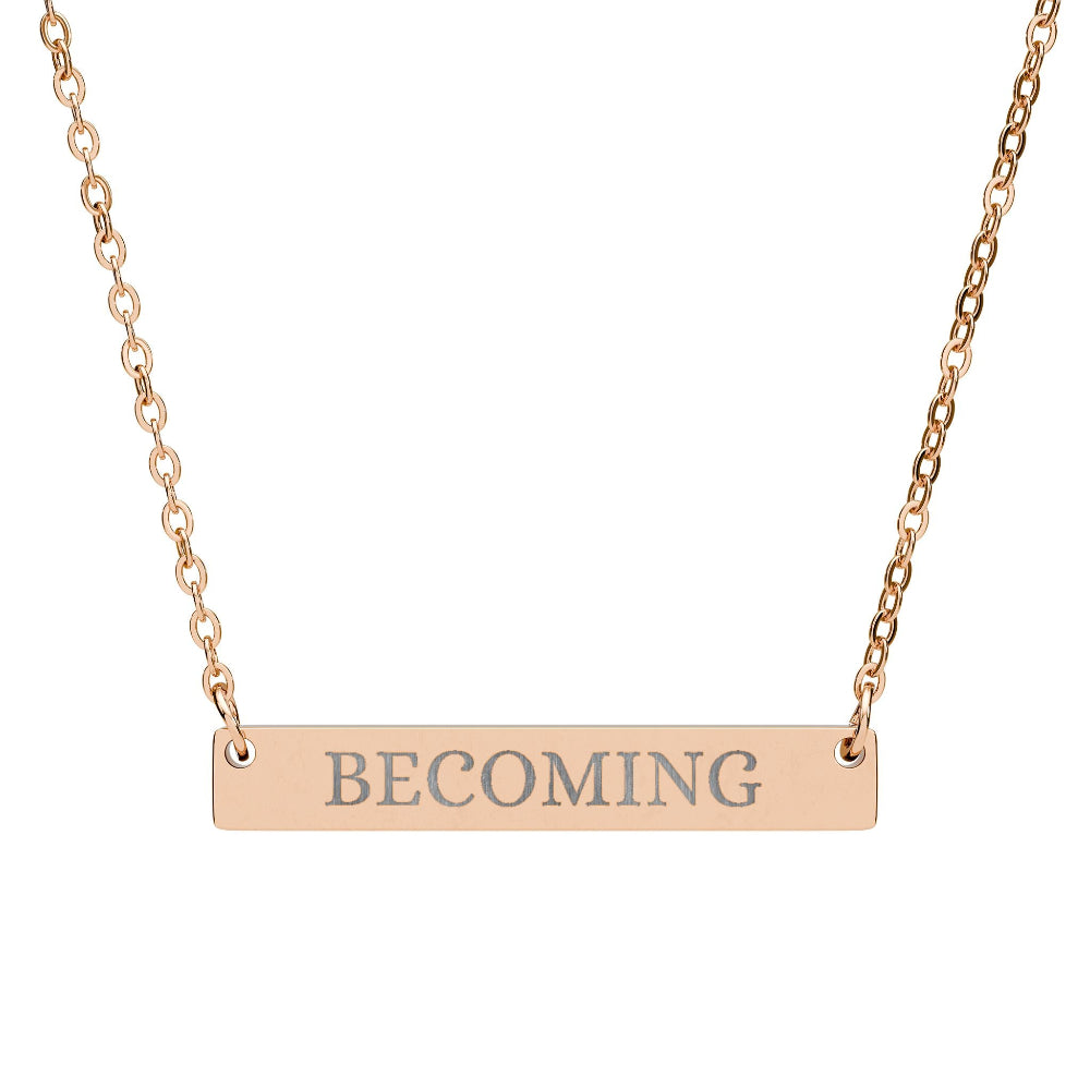 Rose gold bar necklace with engraved uppercase text "BECOMING" on a sleek matte pendant, suspended on a delicate matching rose gold chain. Minimalist motivational affirmation jewelry for growth, transformation, and self-evolution.
