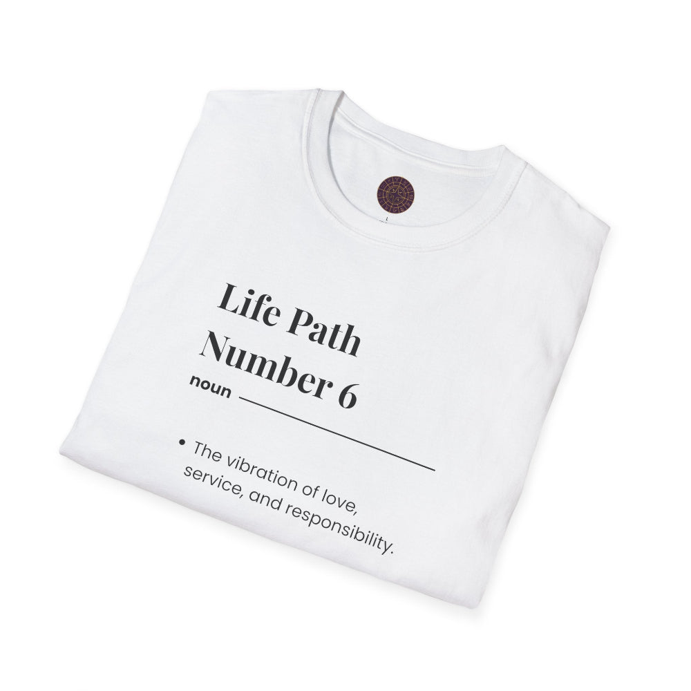 White folded unisex cotton t-shirt featuring bold Life Path Number 6 numerology print: dictionary-style definition of the vibration of love, service, responsibility, harmony, nurturing, family, balance & compassion. Motivational spiritual numerology crewneck tee flat lay with visible purple/gold zodiac wheel inner tag.