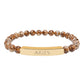 Bracelet with polished leopard jasper beads in earthy brown tones with natural veining, featuring a gold-plated curved bar engraved "ARIES" in uppercase letters. Stretch-fit zodiac-inspired crystal jewelry for passion, courage, and leadership.