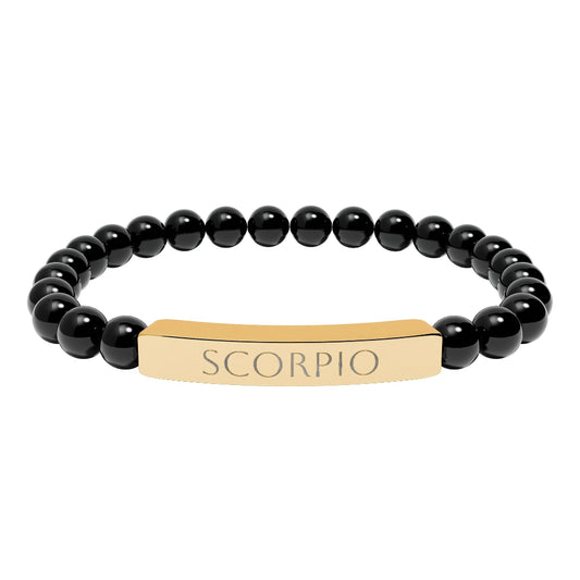 Bracelet with polished black onyx beads and gold-plated curved bar engraved "SCORPIO" in uppercase letters. Stretch-fit zodiac-inspired crystal jewelry for intensity, transformation, and emotional depth.