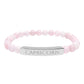 Bracelet with polished rose quartz beads in soft pink tones, natural translucent glow, paired with a silver curved bar engraved "CAPRICORN" in uppercase letters. Stretch-fit zodiac-inspired crystal jewelry.