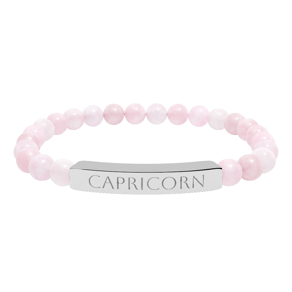 Bracelet with polished rose quartz beads in soft pink tones, natural translucent glow, paired with a silver curved bar engraved "CAPRICORN" in uppercase letters. Stretch-fit zodiac-inspired crystal jewelry.