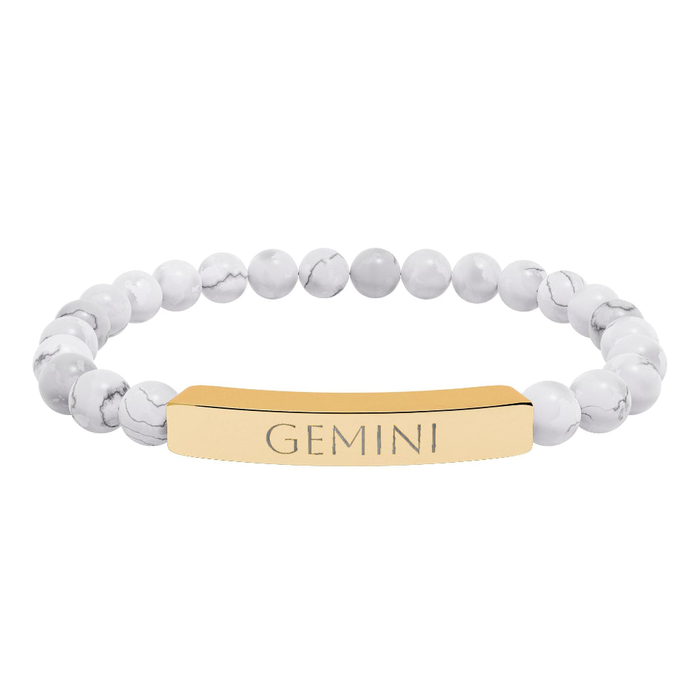 Bracelet with polished white howlite beads featuring natural gray-black veining and marbling, paired with a gold-plated curved bar engraved "GEMINI" in uppercase letters. Stretch-fit zodiac-inspired crystal jewelry.