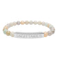 Bracelet with polished pastel beads in soft peach, cream, gray, and light blue tones with natural marbling, featuring a silver curved bar engraved "SAGITTARIUS" in uppercase letters. Stretch-fit zodiac-inspired crystal jewelry.