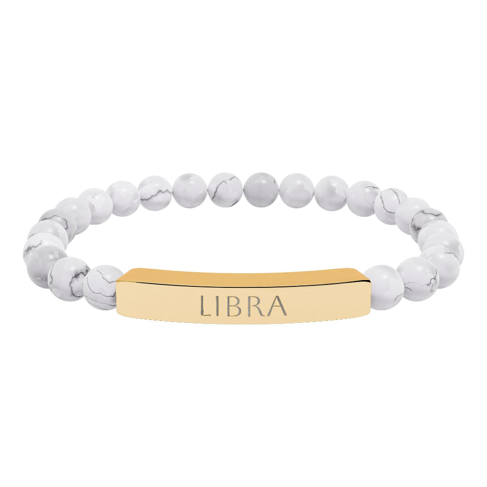 Bracelet with polished white howlite beads featuring natural gray-black veining and marbling, paired with a gold-plated curved bar engraved "LIBRA" in uppercase letters. Stretch-fit zodiac-inspired crystal jewelry for balance, harmony, and relationships.