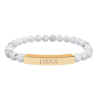 Bracelet with polished white howlite beads featuring natural gray-black veining and marbling, paired with a gold-plated curved bar engraved "LIBRA" in uppercase letters. Stretch-fit zodiac-inspired crystal jewelry for balance, harmony, and relationships.