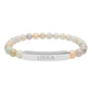 Bracelet with polished pastel beads in soft peach, cream, gray, and light blue tones with natural marbling, featuring a silver curved bar engraved "LIBRA" in uppercase letters. Stretch-fit zodiac-inspired crystal jewelry.