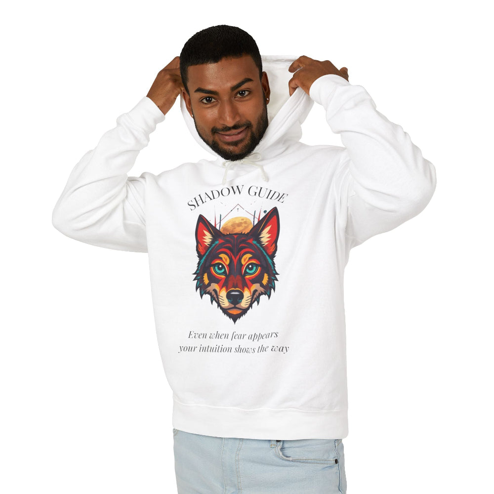 Young man with short hair pulling up the hood of a cream hoodie featuring vibrant multicolored wolf head graphic, intense eyes in orange blue teal splashes, full moon above, "SHADOW GUIDE" arched text, motivational quote about intuition and fear below