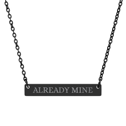 Black bar necklace with engraved uppercase text "ALREADY MINE" on a matte black pendant, suspended on a delicate black chain. Minimalist motivational affirmation jewelry for self-ownership, confidence, and empowerment.