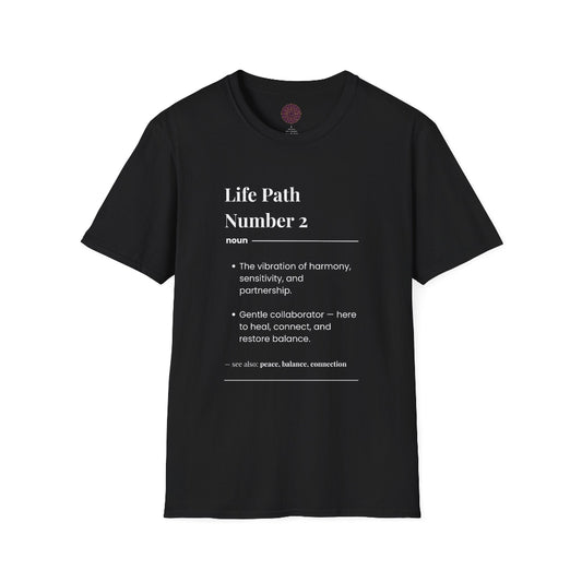Black unisex cotton t-shirt laid out flat featuring bold Life Path Number 2 numerology print in dictionary style: exact text reading "Life Path Number 2 noun · The vibration of harmony, sensitivity, and partnership. · Gentle collaborator — here to heal, connect, and restore balance. – see also: peace, balance, connection". Motivational spiritual numerology crewneck tee flat lay with visible purple/gold zodiac wheel inner tag.