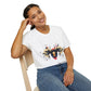 White unisex cotton t-shirt modeled by smiling woman with braided hair, seated pose, hand on cheek, featuring bold Capricorn zodiac graphic: vibrant abstract goat/ram head portrait with large curved horns, intense expression, geometric diamond accents, and dynamic multicolored paint splatters in gold, red, navy, teal, and black tones exploding outward. Elegant black cursive "Capricorn" text below. Astrology zodiac motivational crewneck tee.