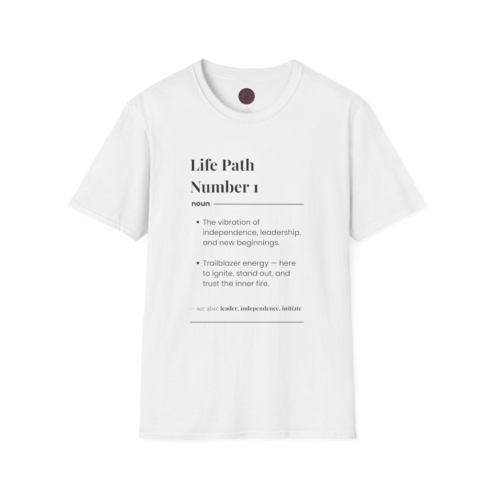 White unisex cotton t-shirt laid out flat featuring bold Life Path Number 1 numerology print in dictionary style: exact text reading “Life Path Number 1 noun · The vibration of independence, leadership, and new beginnings. · Trailblazer energy — here to ignite, stand out, and trust the inner fire. – see also: leader, independence, initiative”. Motivational spiritual numerology crewneck tee flat lay with visible purple/gold zodiac wheel inner tag.