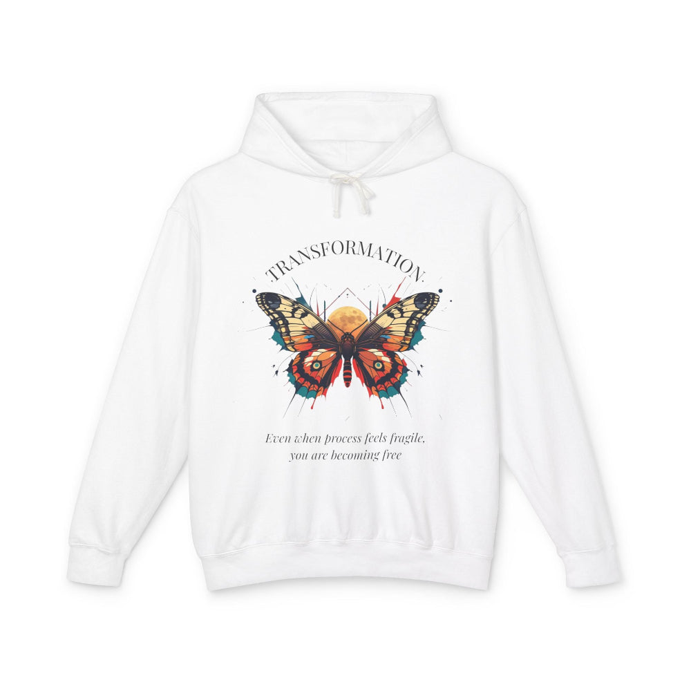 White hoodie featuring colorful abstract butterfly graphic with moon background, "TRANSFORMATION" arched above, and inspirational quote "Even when process feels fragile, you are becoming free" below