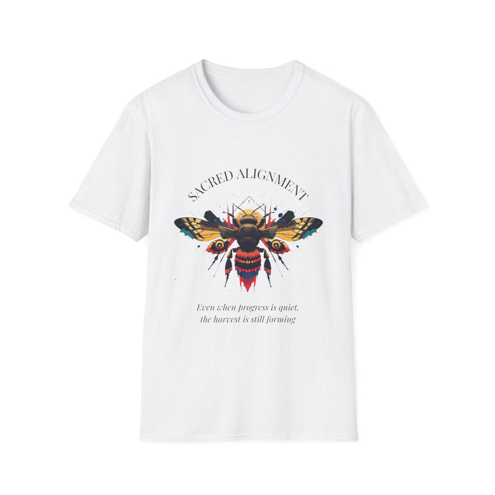 White unisex cotton t-shirt laid out flat featuring bold "Sacred Alignment" graphic: vibrant abstract bee with detailed wings and body, colorful geometric accents, and dynamic paint splatters in red, orange, teal, blue, and gold tones bursting outward around an orange moon background. Arched white text "SACRED ALIGNMENT" above and smaller inspirational quote "Even when progress is quiet, the harvest is still forming" below. Motivational spiritual empowerment crewneck tee.