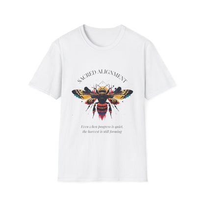 White unisex cotton t-shirt laid out flat featuring bold "Sacred Alignment" graphic: vibrant abstract bee with detailed wings and body, colorful geometric accents, and dynamic paint splatters in red, orange, teal, blue, and gold tones bursting outward around an orange moon background. Arched white text "SACRED ALIGNMENT" above and smaller inspirational quote "Even when progress is quiet, the harvest is still forming" below. Motivational spiritual empowerment crewneck tee.