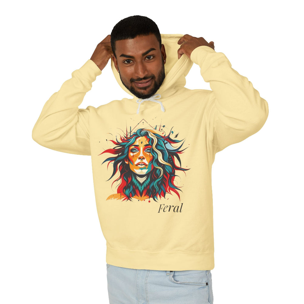 Young man with short hair pulling up the hood of a pale yellow hoodie featuring vibrant artistic portrait of a fierce woman with curly multicolored flowing hair, teal red blue face accents, bold makeup, "Feral" text below
