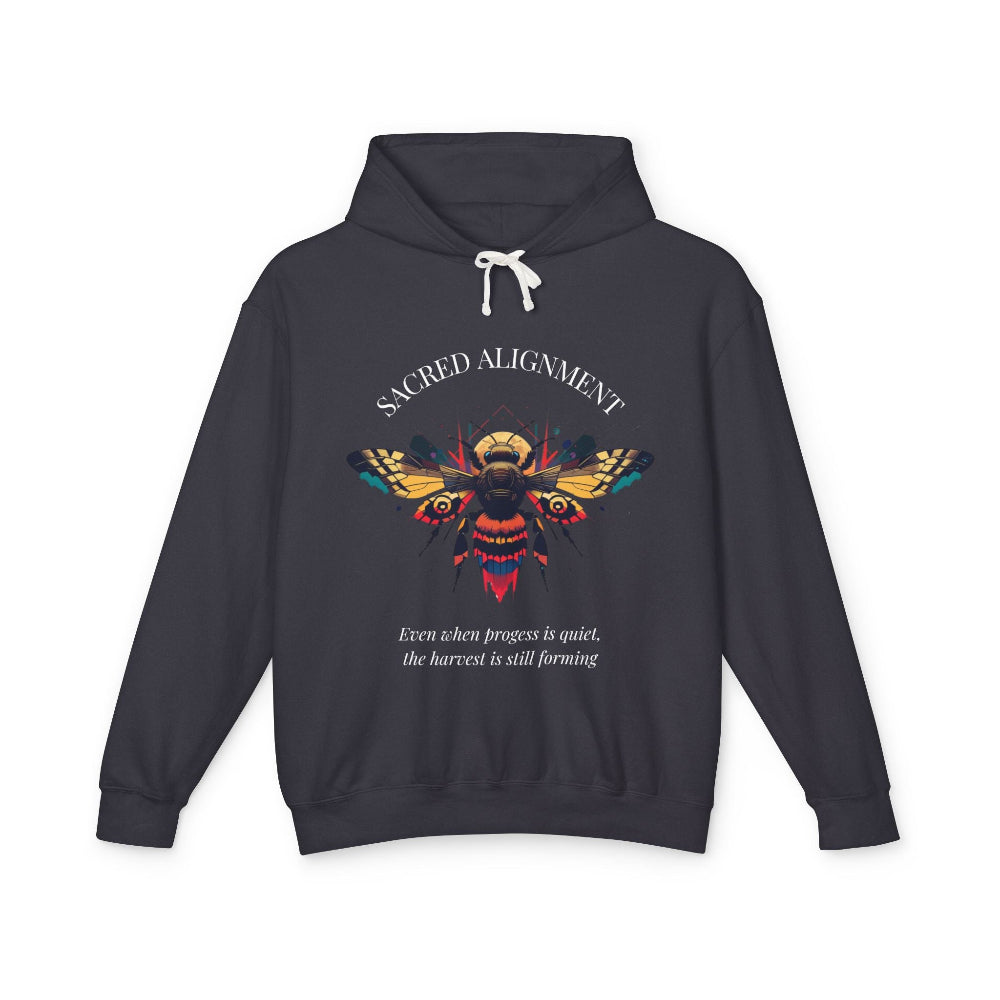 Dark gray hoodie laid flat, featuring a vibrant colorful bee graphic with the text "SACRED ALIGNMENT" arched above and the quote "Even when progress is quiet, the harvest is still forming" below. Motivational streetwear apparel.