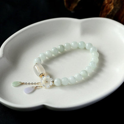 Light green jade bead bracelet with white agate oval, jade teardrop, amethyst drop, and gold-plated plum blossom charm on display