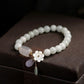 Milky white jade bead bracelet with translucent agate centerpiece, gold plum blossom charm, and jade-amethyst teardrop pendants on dark wood stand