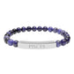 Bracelet with polished lapis lazuli and black onyx beads in deep blue and black tones, featuring a silver curved bar engraved "PISCES" in uppercase letters. Stretch-fit zodiac-inspired crystal jewelry.