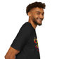 Black unisex cotton t-shirt in side profile on smiling male model with curly hair and beard, featuring bold Year of the Rat graphic on chest: vibrant abstract rat face portrait with large ears, intense eyes, geometric patterns, and multicolored paint splatters in yellow, red, blue, teal, and orange. Chinese text "鼠年" (Year of the Rat) printed below in white. Zodiac Chinese New Year motivational crewneck tee.