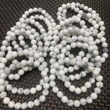 White howlite gemstone bead strands with natural gray marble veining, round polished beads arranged on a dark woven background.
