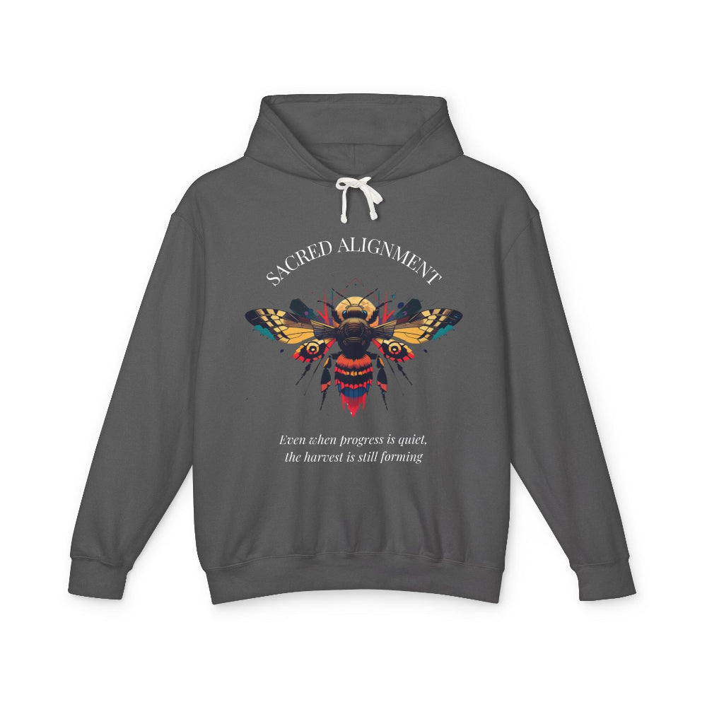 Gray hoodie laid flat, featuring a vibrant colorful bee graphic with the text "SACRED ALIGNMENT" arched above and the quote "Even when progress is quiet, the harvest is still forming" below. Motivational streetwear apparel.