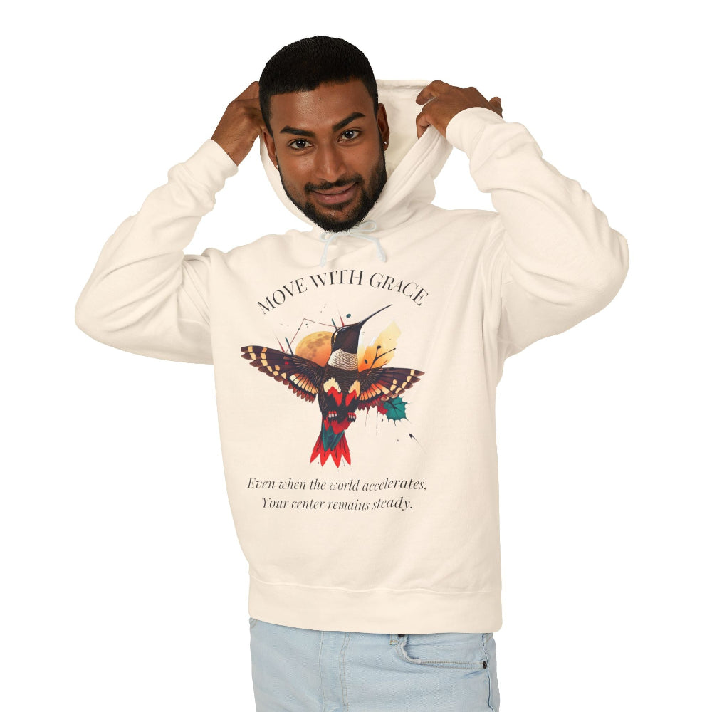 Man modeling a cream hoodie with 'Move With Grace' inspirational hummingbird graphic and quote 'Even when the world accelerates, Your center remains steady' printed on the front.