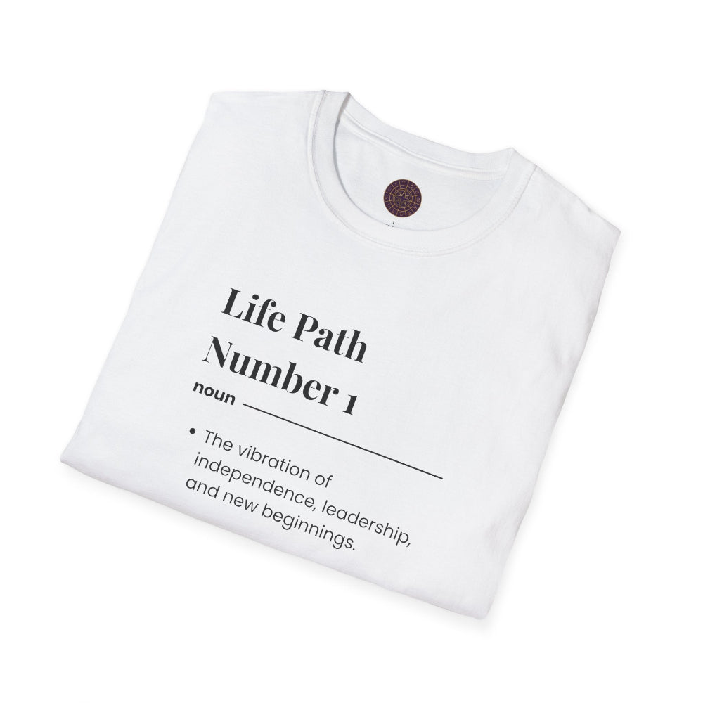 White folded unisex cotton t-shirt featuring bold Life Path Number 1 numerology print in dictionary style: exact text reading "Life Path Number 1 noun · The vibration of independence, leadership, and new beginnings." Motivational spiritual numerology crewneck tee flat lay with visible purple/gold zodiac wheel inner tag.