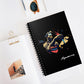 Black spiral-bound notebook featuring a vibrant Aquarius zodiac illustration of a water bearer pouring water in gold, blue, and red tones with abstract splashes, “Aquarius” written in white script at the bottom, styled on a clean desk with sunglasses and stationery items.