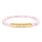 Bracelet with polished rose quartz beads in soft pink tones, natural translucent glow, paired with a gold-plated curved bar engraved "PISCES" in uppercase letters. Stretch-fit zodiac-inspired crystal jewelry.