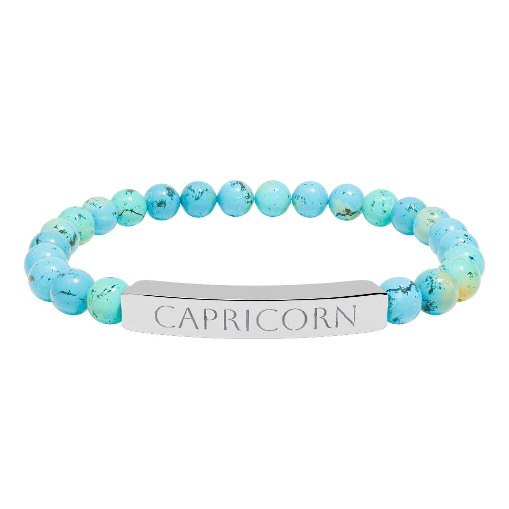 Bracelet with polished turquoise beads in soft aqua-blue tones with natural veining and speckles, featuring a silver curved bar engraved "CAPRICORN" in uppercase letters. Stretch-fit zodiac-inspired crystal jewelry.