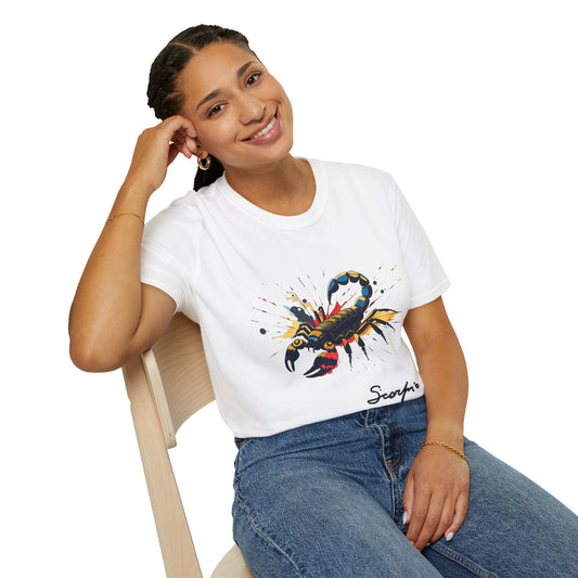 White unisex cotton t-shirt modeled by smiling woman with braided hair, seated pose, hand on cheek, featuring bold Scorpio zodiac graphic on chest: vibrant abstract scorpion silhouette with raised stinger, intense glowing eyes, detailed tail and pincers, geometric patterns, and explosive multicolored paint splatters in gold, red, navy, teal, and black tones bursting outward. Elegant black cursive "Scorpio" text below. Astrology zodiac motivational crewneck tee.