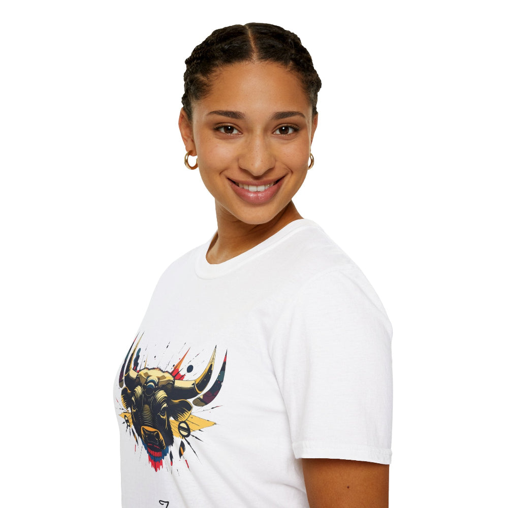 White unisex cotton t-shirt in side profile on smiling woman with braided hair, featuring bold Year of the Ox graphic on chest: vibrant abstract ox/bull face portrait with large curved horns, intense expression, geometric patterns, and dynamic multicolored paint splatters in gold, red, navy, teal, and black tones exploding outward. Elegant black cursive "Taurus" text below. Astrology zodiac motivational crewneck tee.