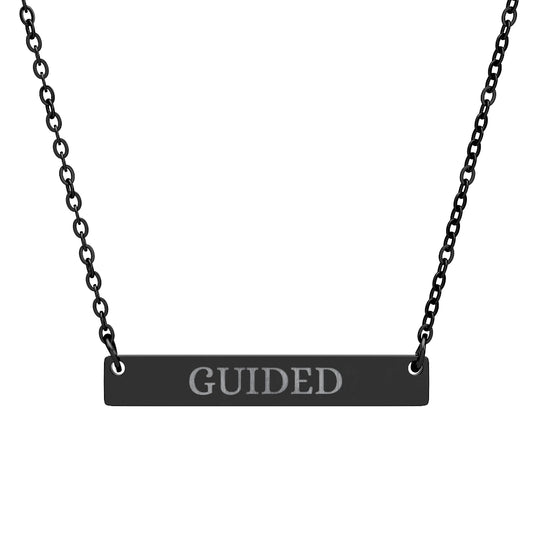 Black bar necklace with engraved uppercase text "GUIDED" on a matte black pendant, suspended on a delicate black chain. Minimalist motivational affirmation jewelry for guidance, intuition, and spiritual alignment.