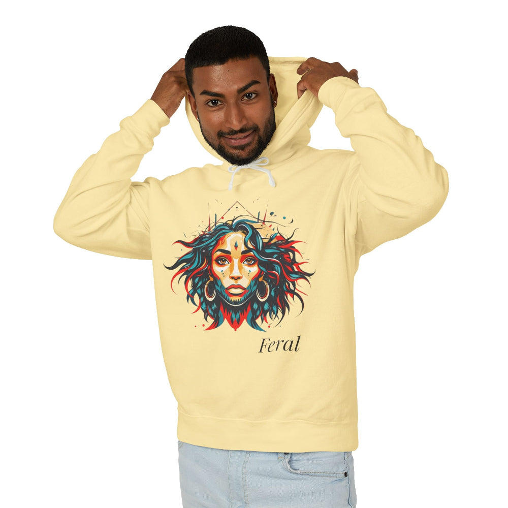 Young man with short hair pulling up the hood of a pale yellow hoodie featuring vibrant artistic portrait of a fierce woman with curly multicolored flowing hair, teal red blue orange face accents, large hoop earrings, third-eye symbol, "Feral" text below