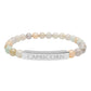 Bracelet with polished pastel beads in soft peach, cream, gray, and light blue tones with natural marbling, featuring a silver curved bar engraved "CAPRICORN" in uppercase letters. Stretch-fit zodiac-inspired crystal jewelry.