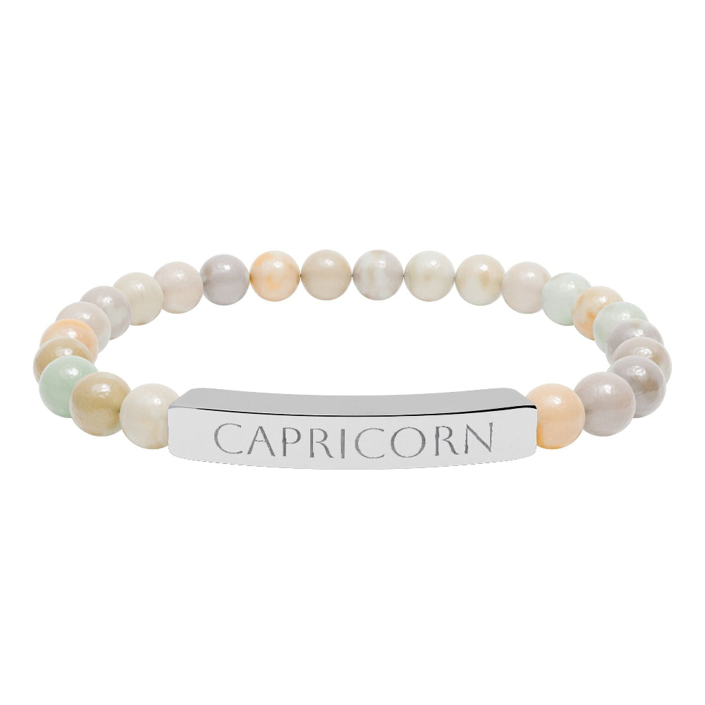 Bracelet with polished pastel beads in soft peach, cream, gray, and light blue tones with natural marbling, featuring a silver curved bar engraved "CAPRICORN" in uppercase letters. Stretch-fit zodiac-inspired crystal jewelry.